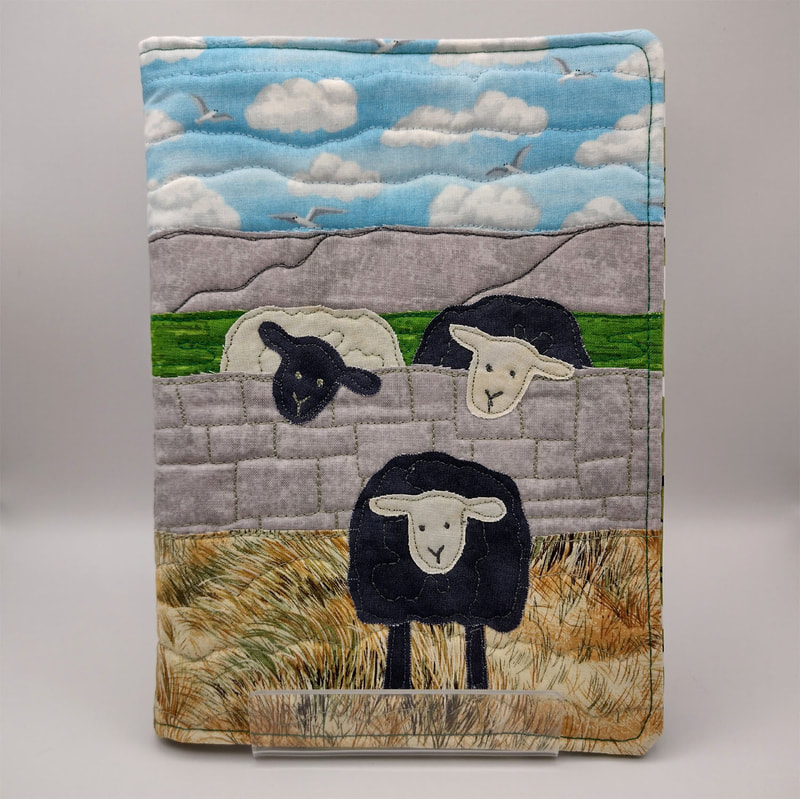 picture of a quilted  book cover with three quirky sheep in a landscape design